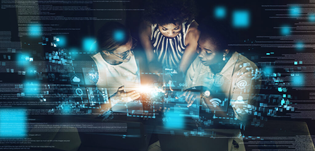 Three women around a computer smiling and pointing toward the screen - futuristic setting.